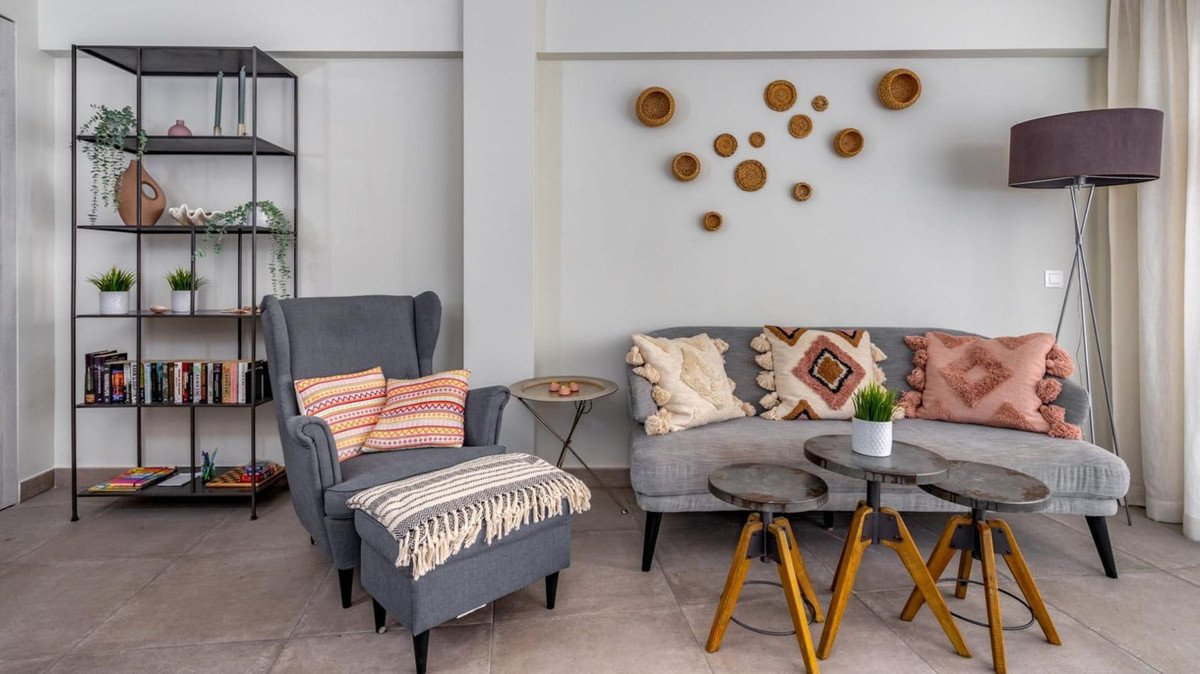 A cozy living room with a grey sofa, armchair, a metal shelf, and decorative wall baskets.