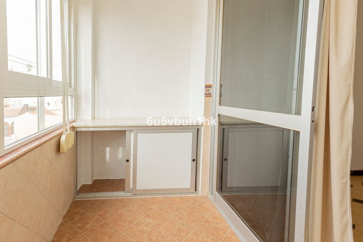 A small balcony area with built-in storage cabinets with sliding doors and large windows overlooking buildings.