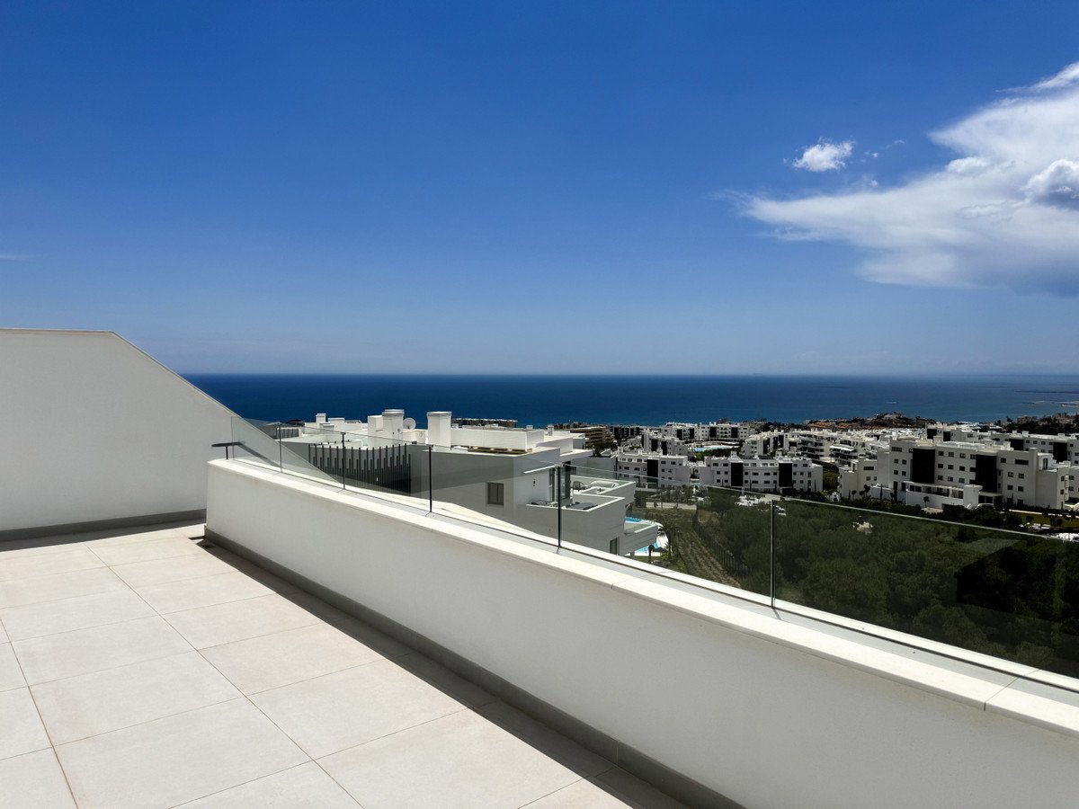 Rooftop terrace with white tiles and glass railing overlooking the sea and city.