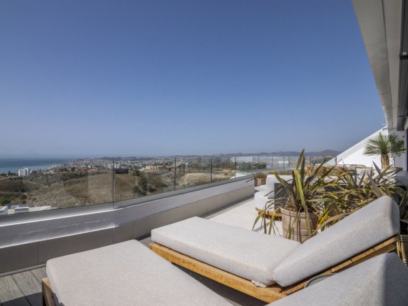 Spacious terrace with lounge chairs and a panoramic sea and city view under a clear blue sky.