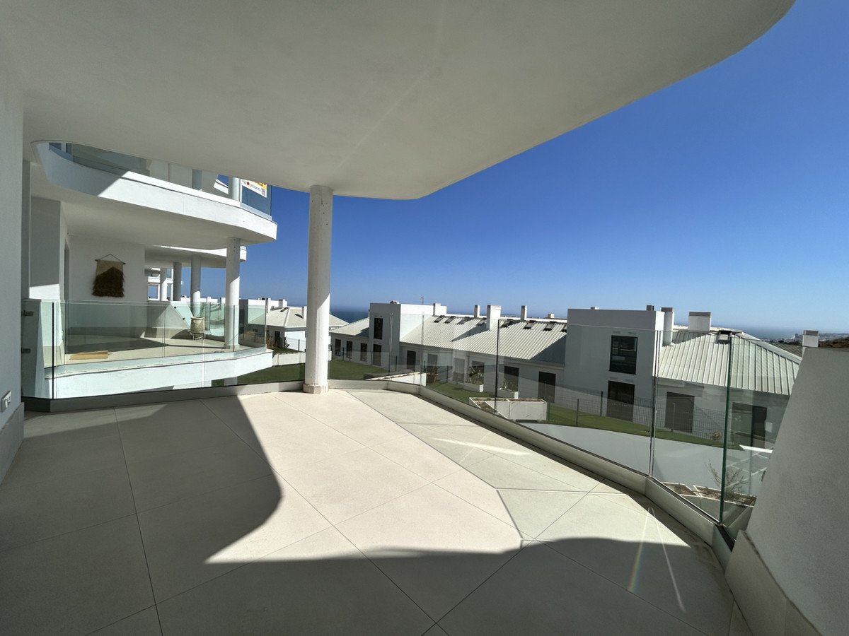 Spacious modern balcony with glass railings offering a clear view of the sea and surrounding contemporary buildings.