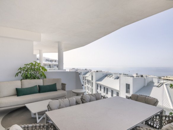 Modern terrace with sofa and dining table offering a beautiful sea view and white building landscape.