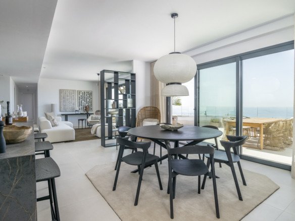 Modern dining area with black chairs and table, offering a beautiful sea view and balcony access.