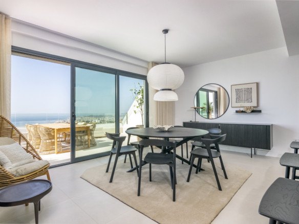 Modern dining room with a round table and chairs, featuring large sliding glass doors with a sea view and access to an outdoor dining area.