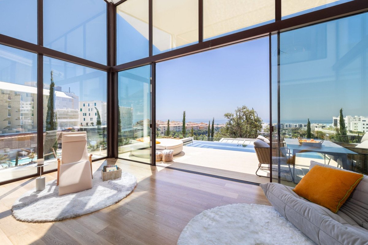 Modern living room with floor-to-ceiling windows opening to a patio, swimming pool, and panoramic sea view.