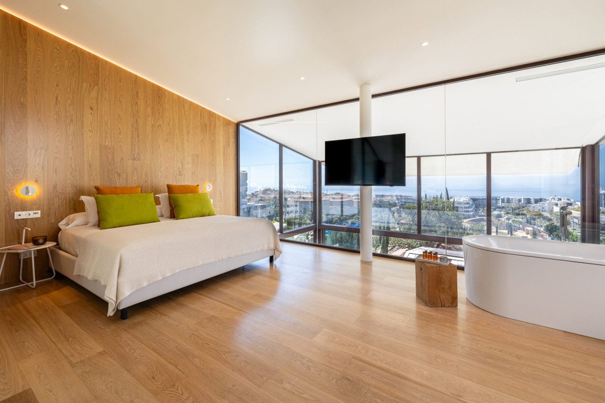 Luxurious bedroom with a king-size bed, large windows offering an ocean view, a TV, and a freestanding bathtub.