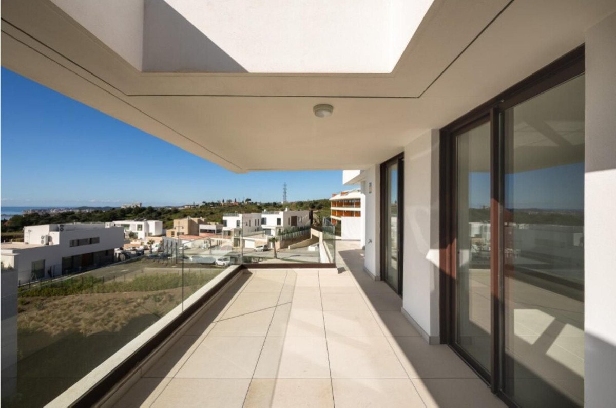 Modern balcony with glass railings offering a panoramic view of the sea and contemporary architecture under a clear blue sky.