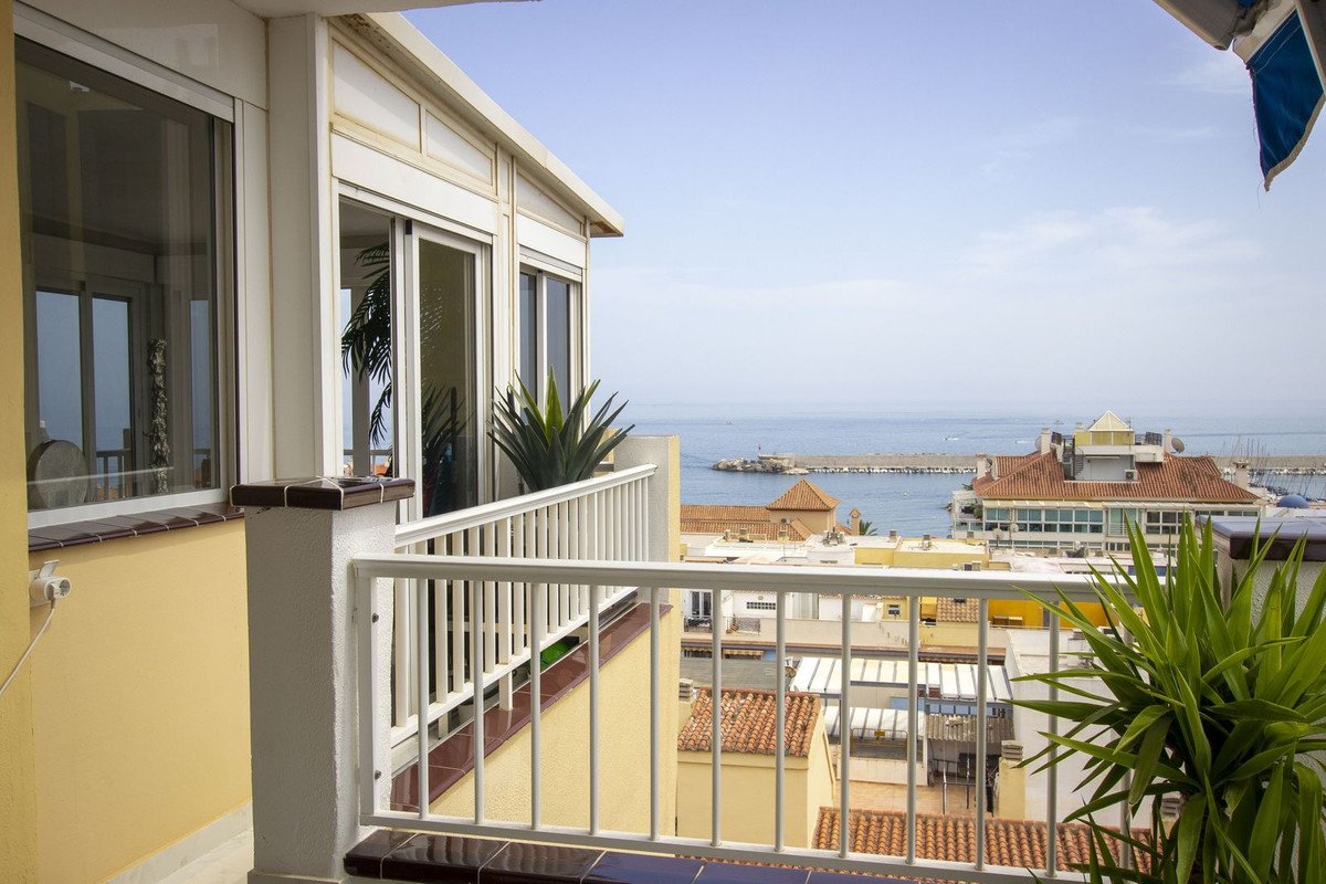 View from a balcony overlooking the sea, rooftops, and a harbor.