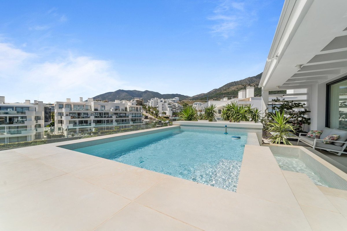 Modern terrace with infinity pool overlooking the sea, with mountainous landscape and modern buildings in the background.