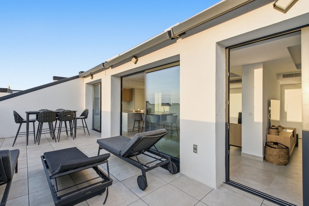 Modern outdoor terrace with lounge chairs, dining table, and view into a contemporary kitchen and living area.