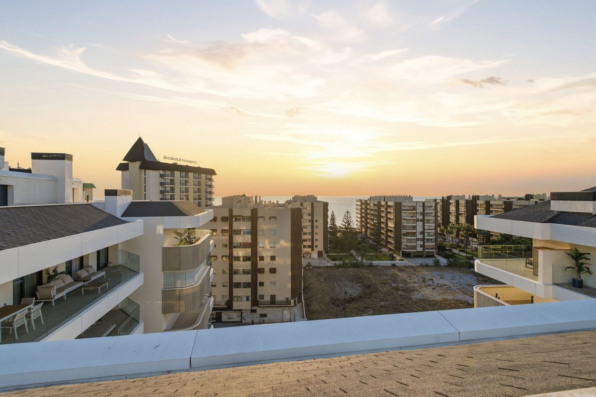 Balcony view of apartments and the sea at sunset, with modern architecture and outdoor seating.