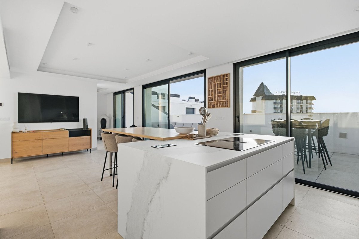 Modern open-plan kitchen and dining area with island, leading to a spacious terrace with outdoor seating and a distant building view.