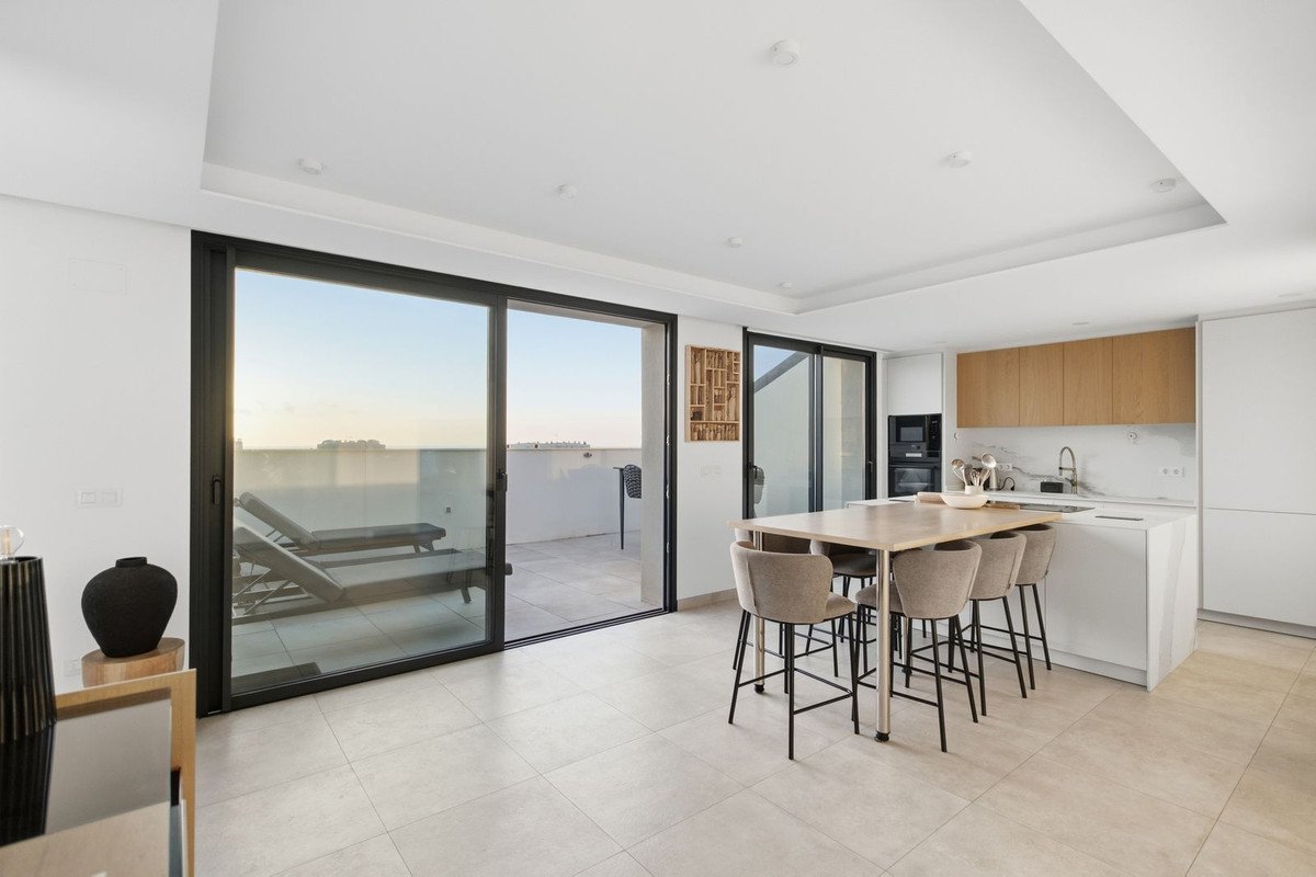Modern open-plan living space with kitchen, dining area, and sliding doors leading to a terrace with lounge chairs and an open view.