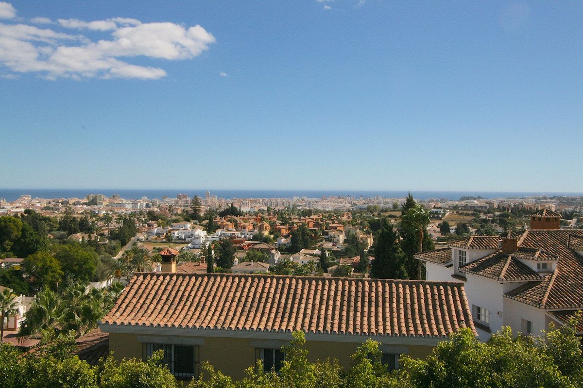 Expansive view of a coastal city with rooftops in the foreground and the blue sea in the distance under a clear sky.