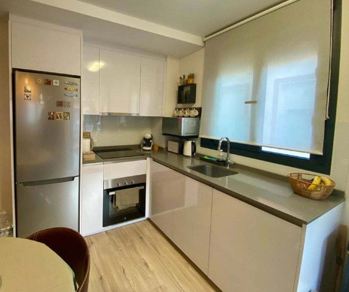 A modern kitchen featuring white cabinets, stainless steel appliances including a refrigerator and oven, a sink, and a large window with blinds.