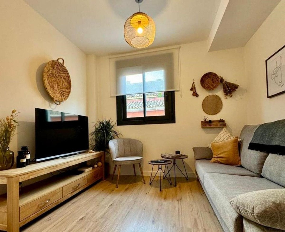 Cozy living room with a grey sofa, TV, decorative wall hangings, and a large window.