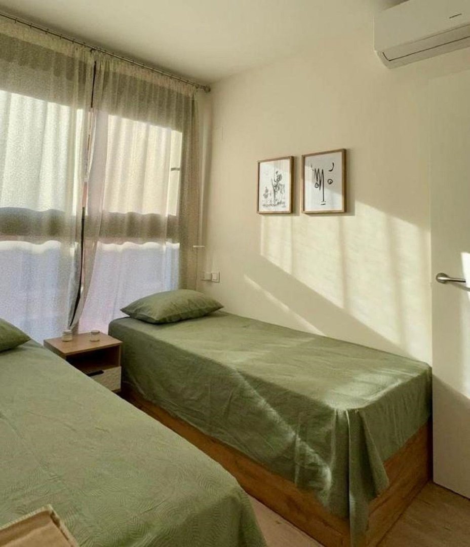 A bedroom with two twin beds, natural light streaming through the window, and minimalist art on the wall.