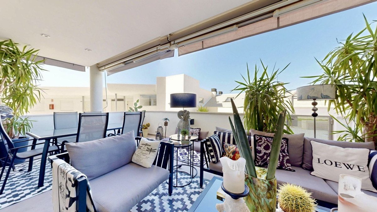 Spacious terrace with dining table, lounge seating, lush plants, and city views under a retractable awning.