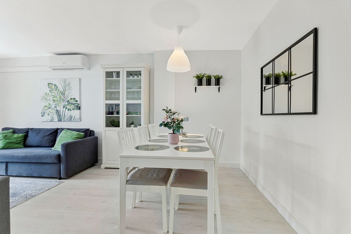 Modern living and dining room with blue sofa, white table, and green accents