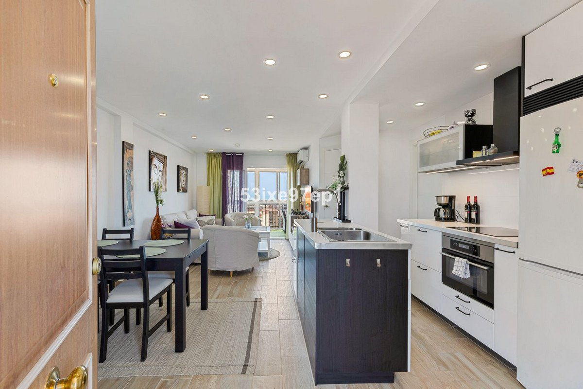 Open-plan living, dining, and kitchen area with a modern island, leading to a balcony with city views.