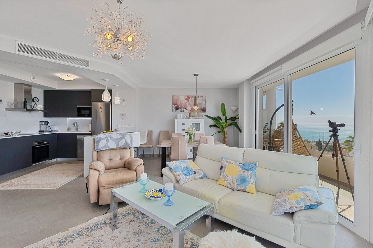 Bright living and dining area with a modern kitchen, white leather sofa, and a beautiful sea view from the balcony.