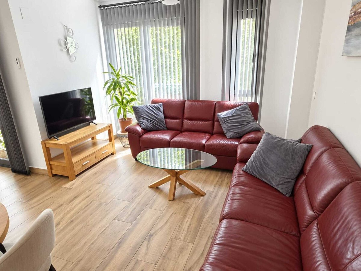 A modern living room featuring a red leather sectional sofa, glass coffee table, TV, and large windows with a green outdoor view.