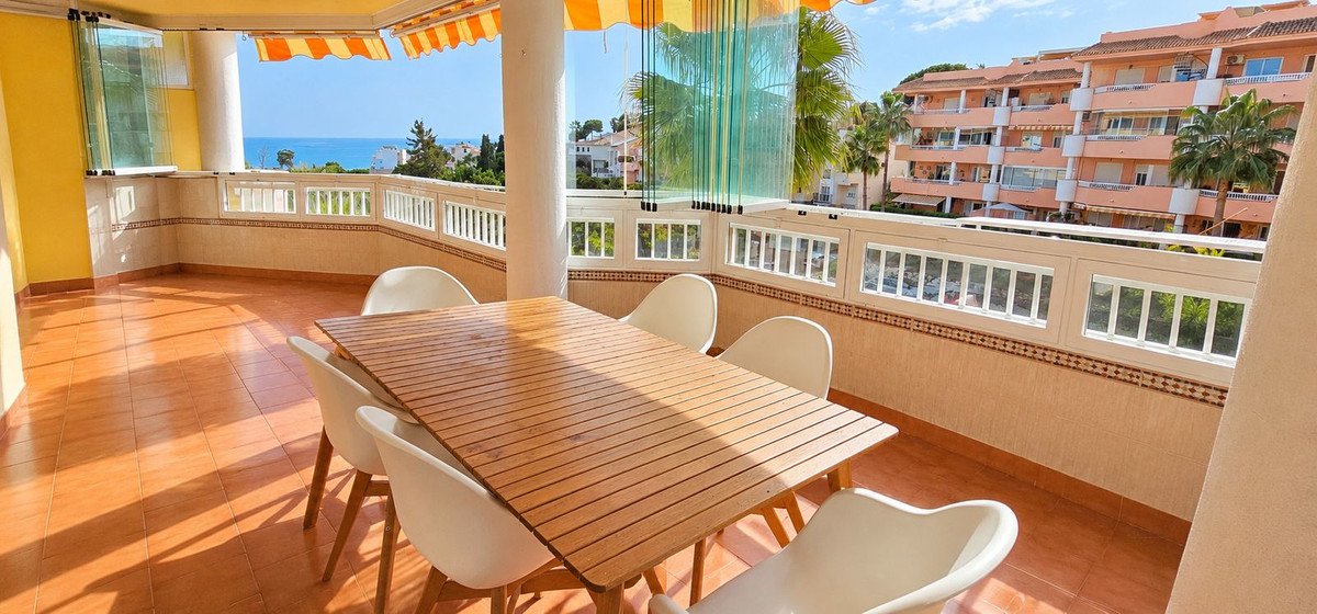 Balcony dining area with wooden table, white chairs, and sea view