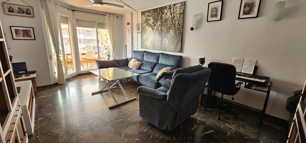 A living room with a blue sofa, glass coffee table, and piano near sliding doors.