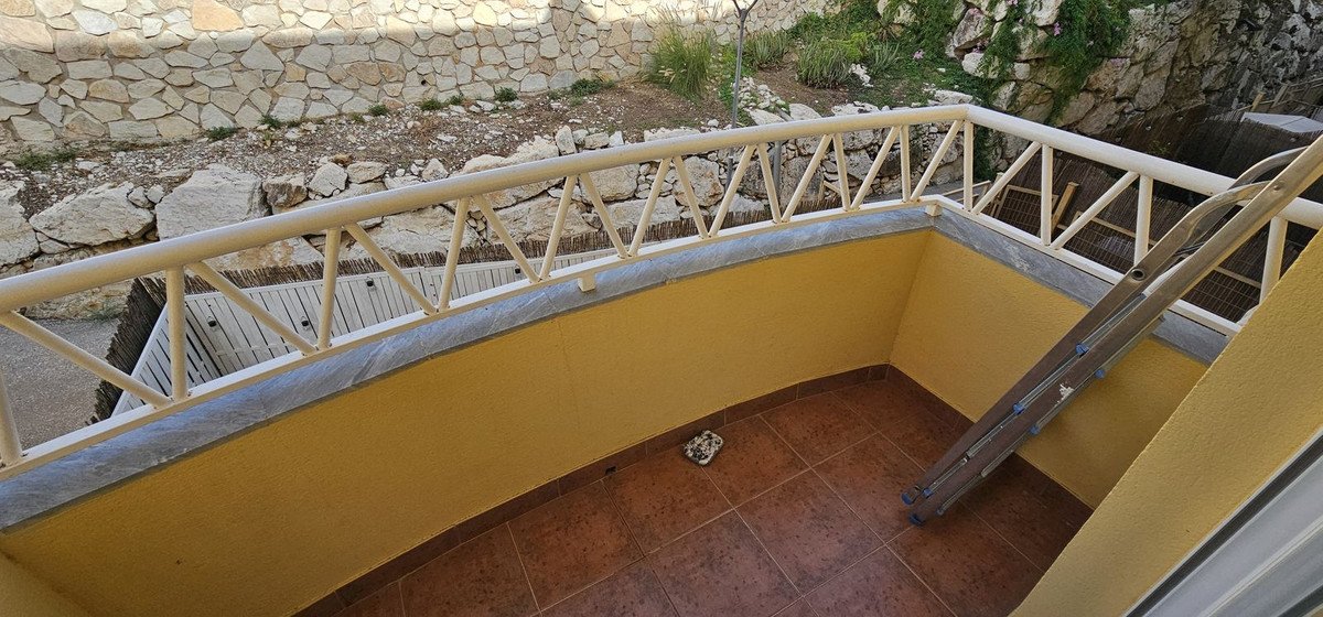 A balcony with a ladder, yellow walls, and a stone wall view