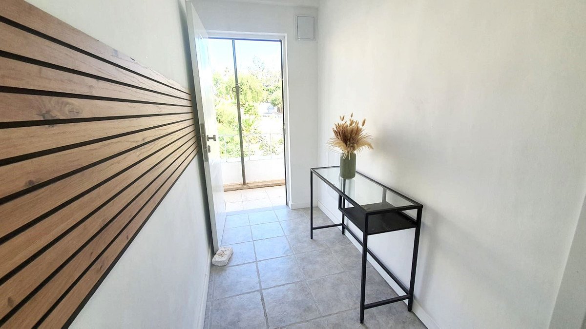 Modern entryway with wooden slat wall, glass console table, and door to balcony with greenery view.