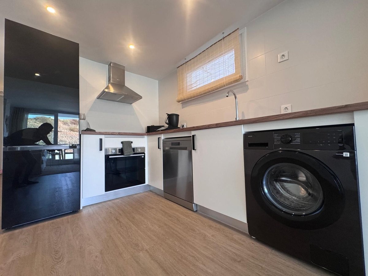 Modern kitchen with a black refrigerator, oven, dishwasher, and washing machine. Features a window above the sink.