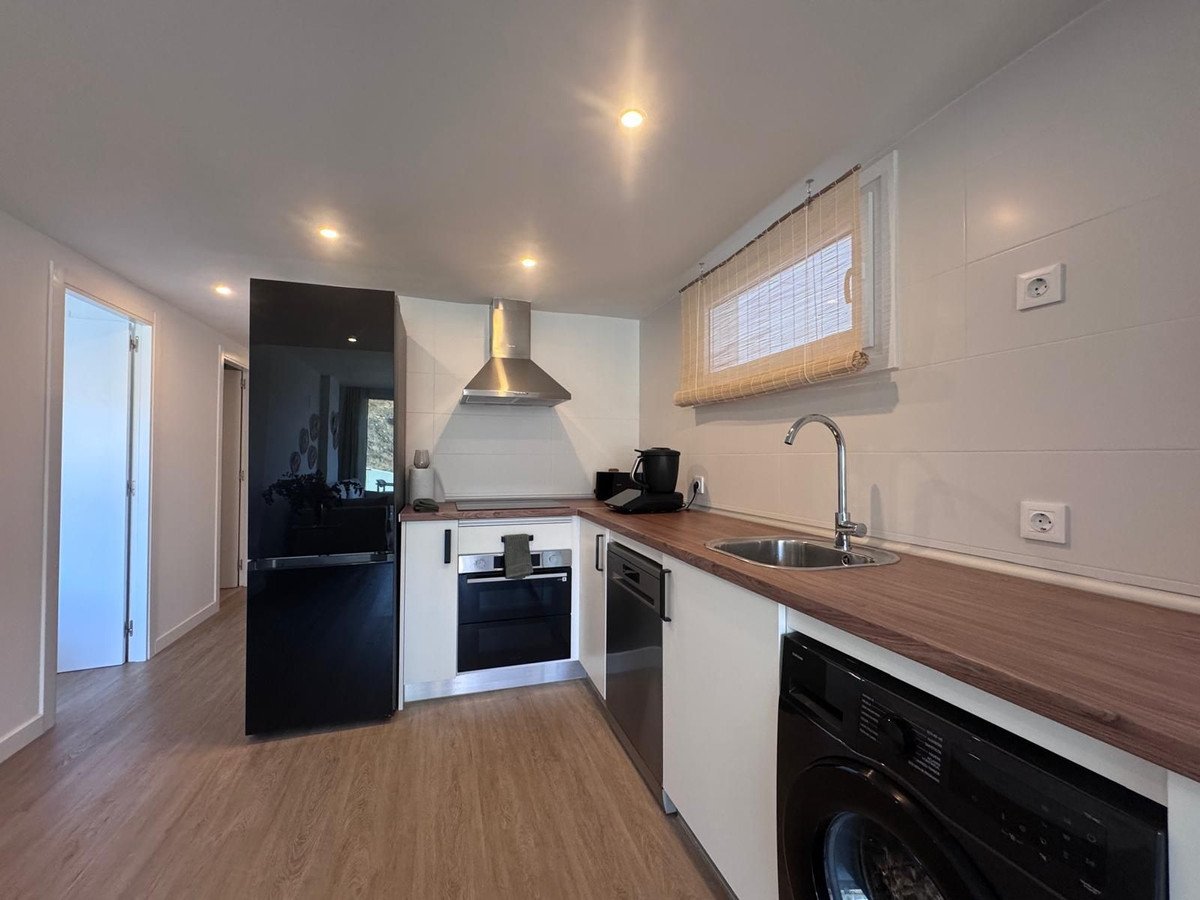 A modern kitchen with stainless steel appliances, including a refrigerator, oven, and washing machine, under bright ceiling lights.