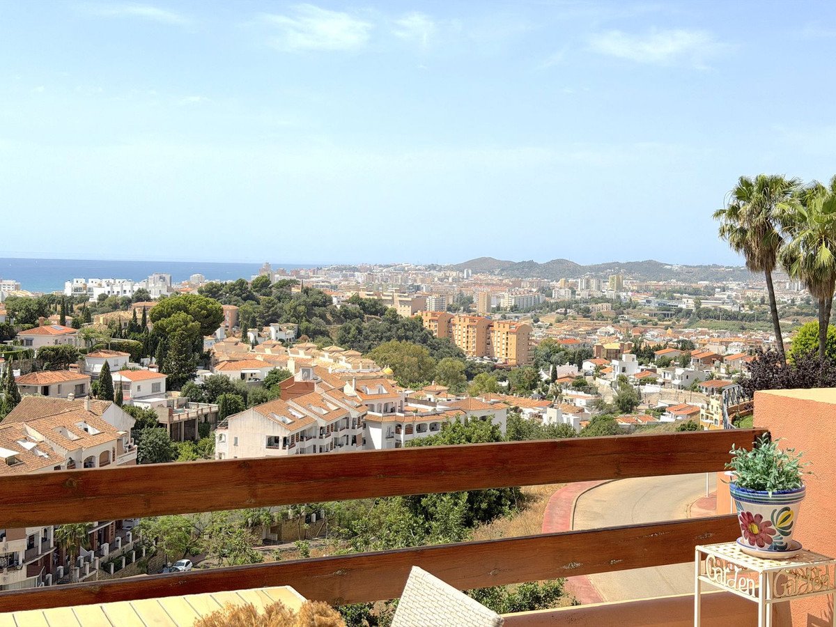 A scenic balcony view overlooking a coastal city with palm trees and the sea in the distance under a clear blue sky.