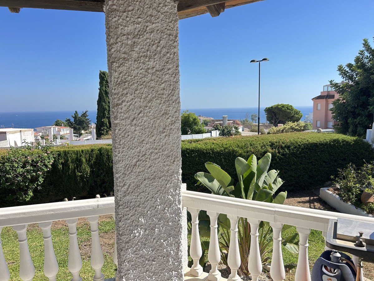 Balcony view with the Mediterranean Sea in the background, lush green gardens, and a white railing.