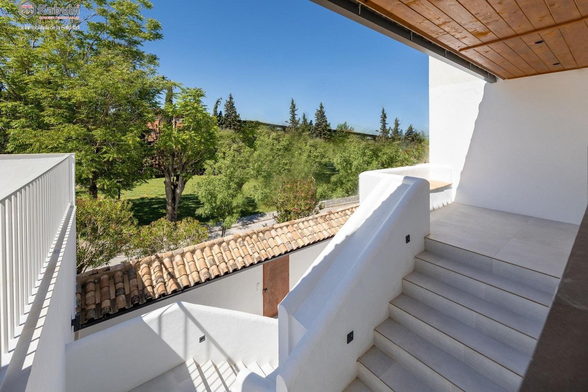 A white modern staircase leads to a terrace with a lush green garden view under a clear blue sky.