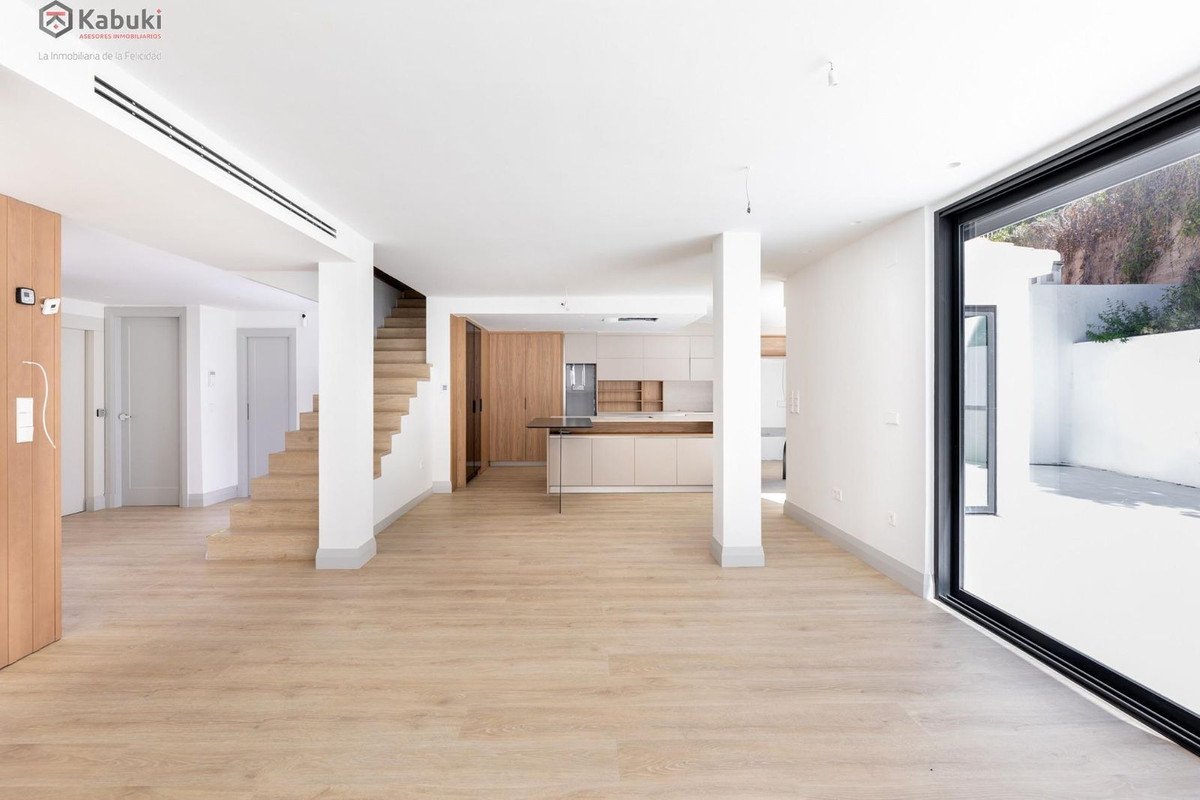 Spacious modern living area with an open-plan kitchen and a staircase leading upstairs. Large window offers outdoor view.