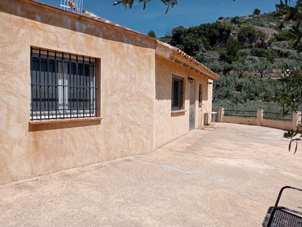 Exterior view of a house with a terrace overlooking hills and greenery under a clear sky.