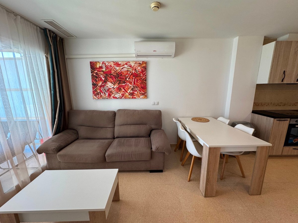 Modern living and dining area with brown sofa, white table, chairs, and abstract art on the wall.