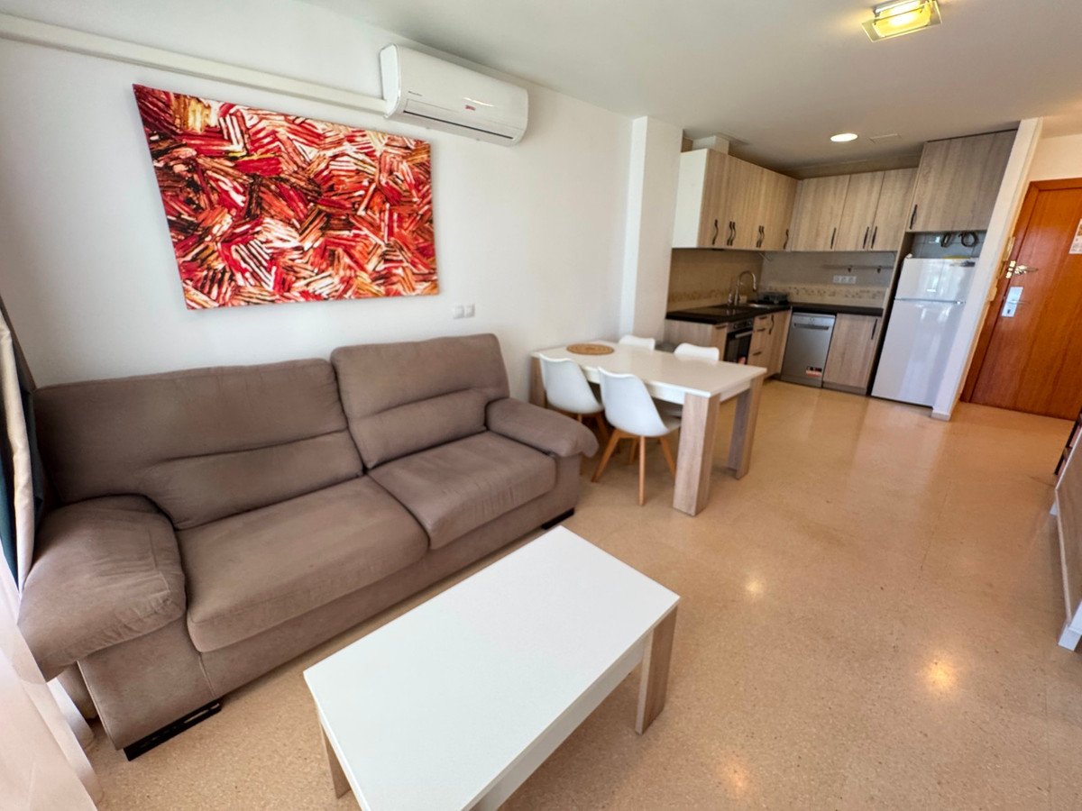 A modern living area with a sofa, coffee table, dining table, and kitchenette. Decorated with abstract art and an air conditioning unit.