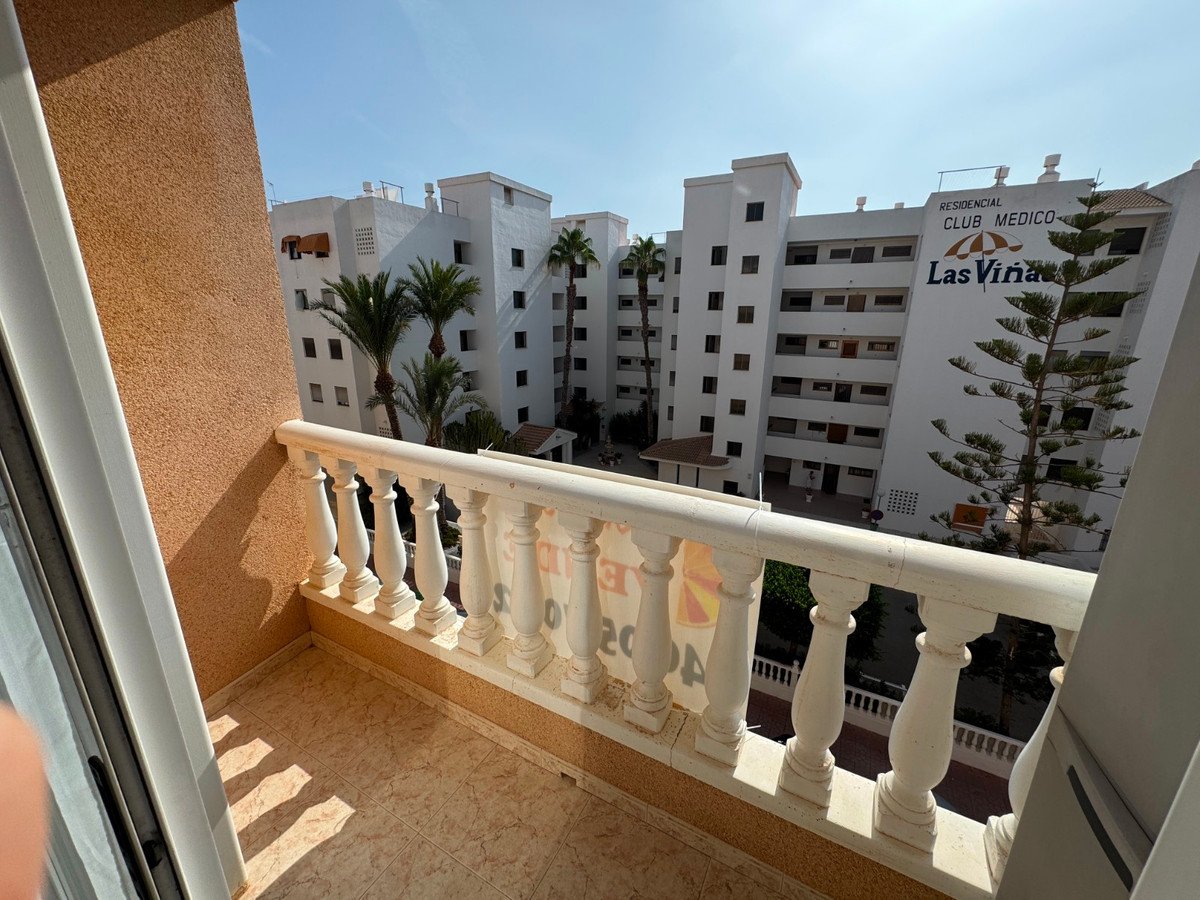 View from balcony overlooking apartment buildings with palm trees and a clear blue sky.