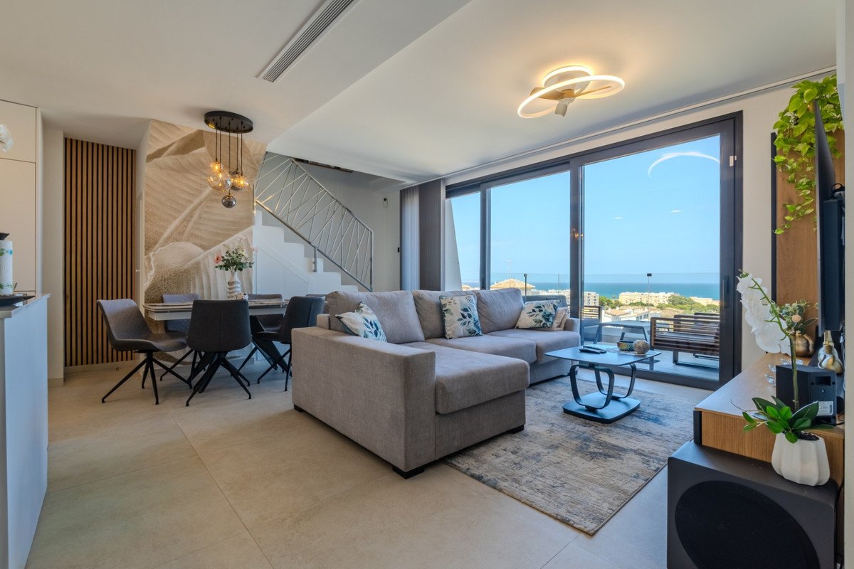 Modern living and dining area with a large sectional sofa, dining table, and floor-to-ceiling windows offering a sea view.