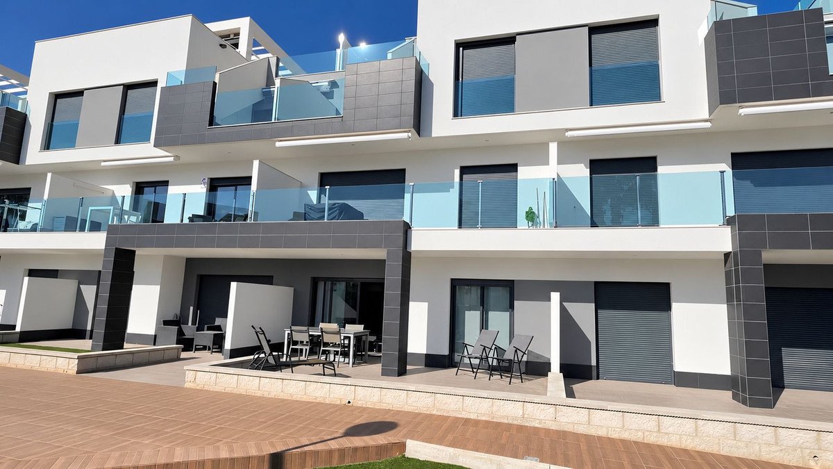 Modern apartments with multiple levels, balconies featuring glass railings, and ground-level patios with outdoor seating.