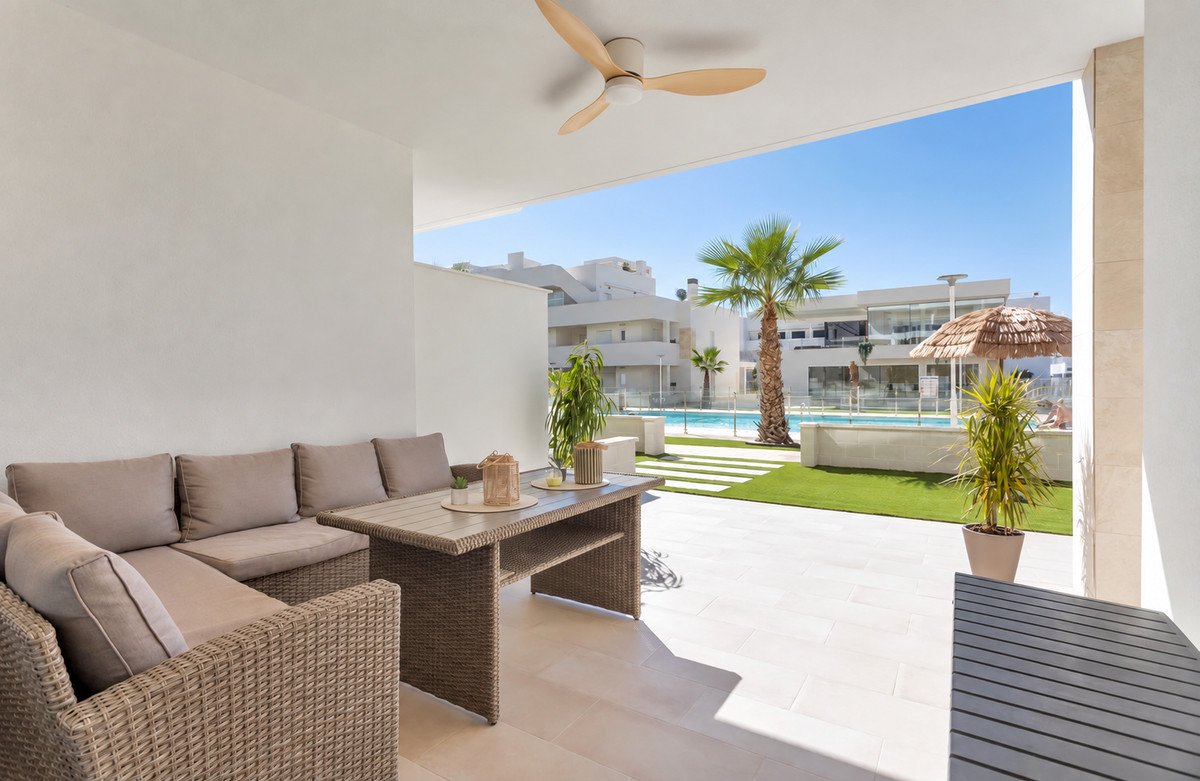 Outdoor terrace with a comfortable sofa and dining table, overlooking a swimming pool and palm trees on a sunny day.