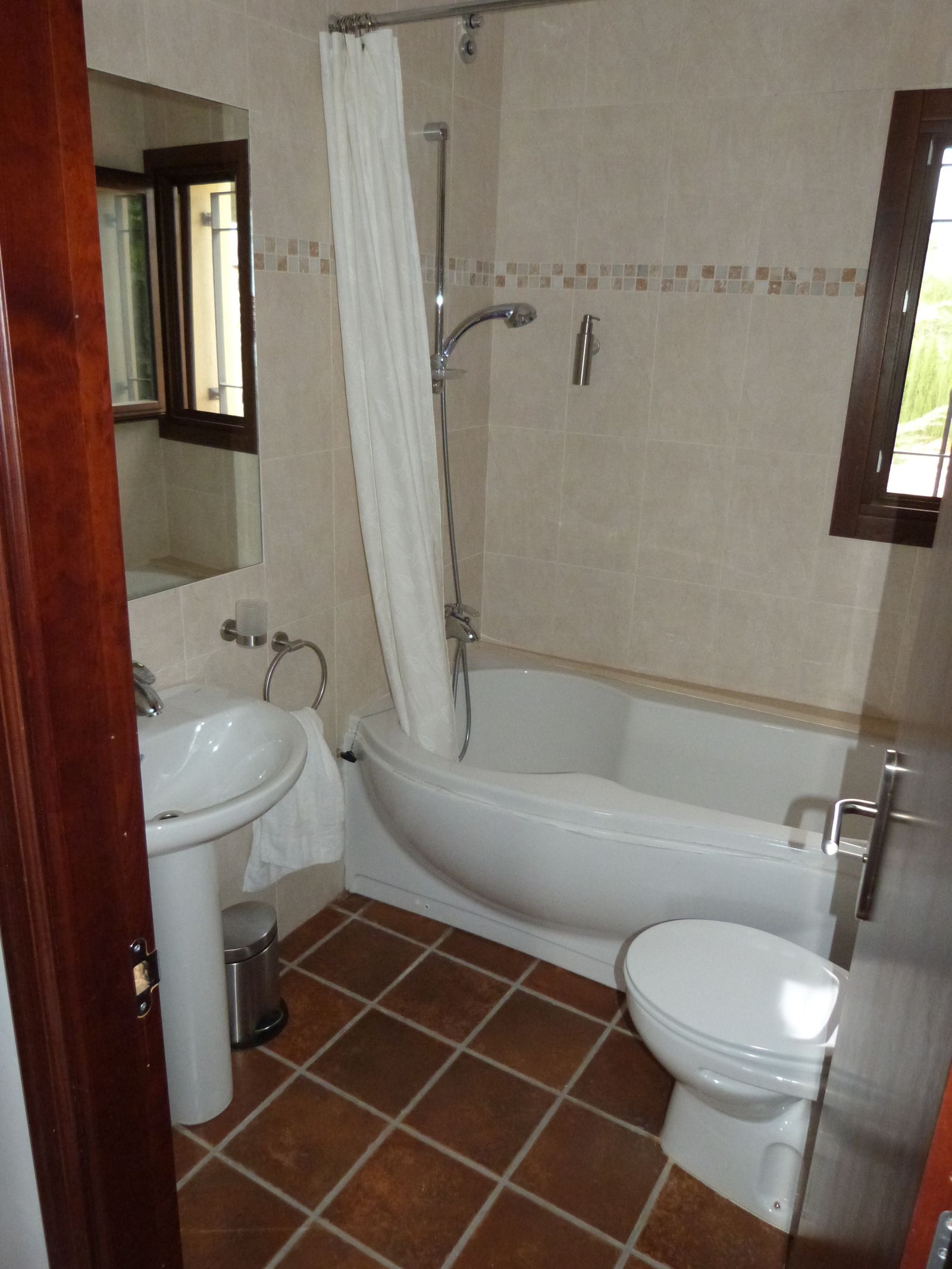 Badkamer met bad, toilet en bruine tegels.