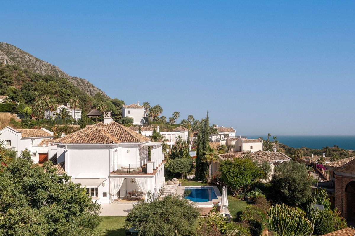 A white villa with a swimming pool and lush garden, overlooking the sea on a sunny day.
