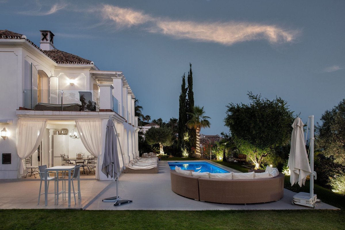 Luxury villa with a swimming pool and a large outdoor seating area, illuminated at dusk with white curtains hanging by the entrance.