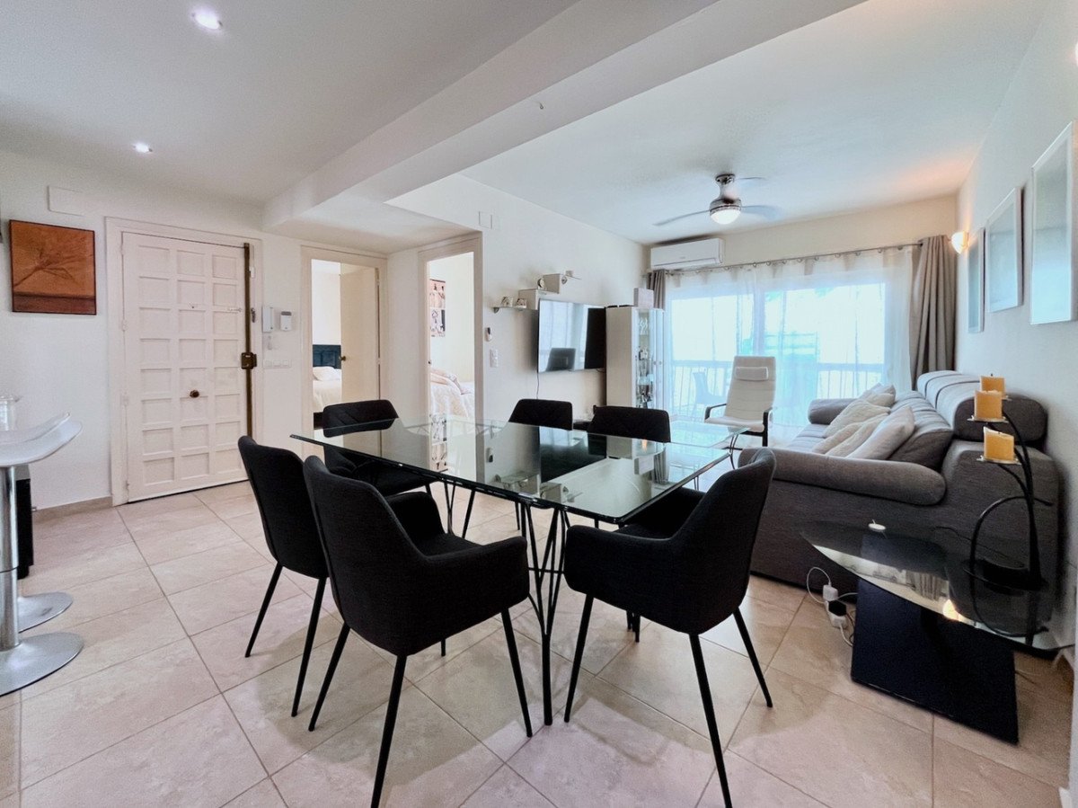 A modern dining area with a glass table and chairs, adjacent to a living room with a sofa and large windows.