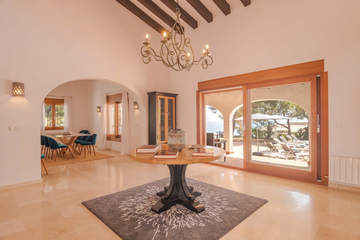 Spacious foyer with a round table, leading to a patio with lounge chairs and a beautiful sea view.
