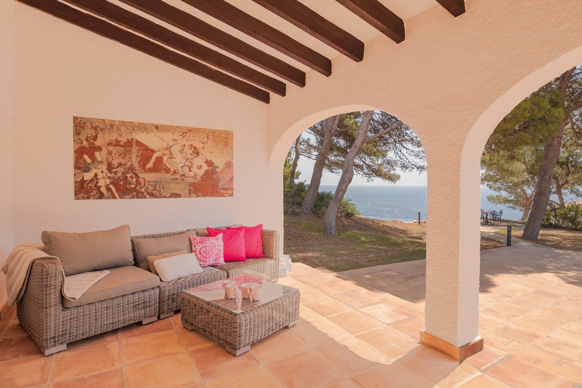 Covered terrace with wicker seating and a coffee table, featuring a beautiful sea view through an archway.