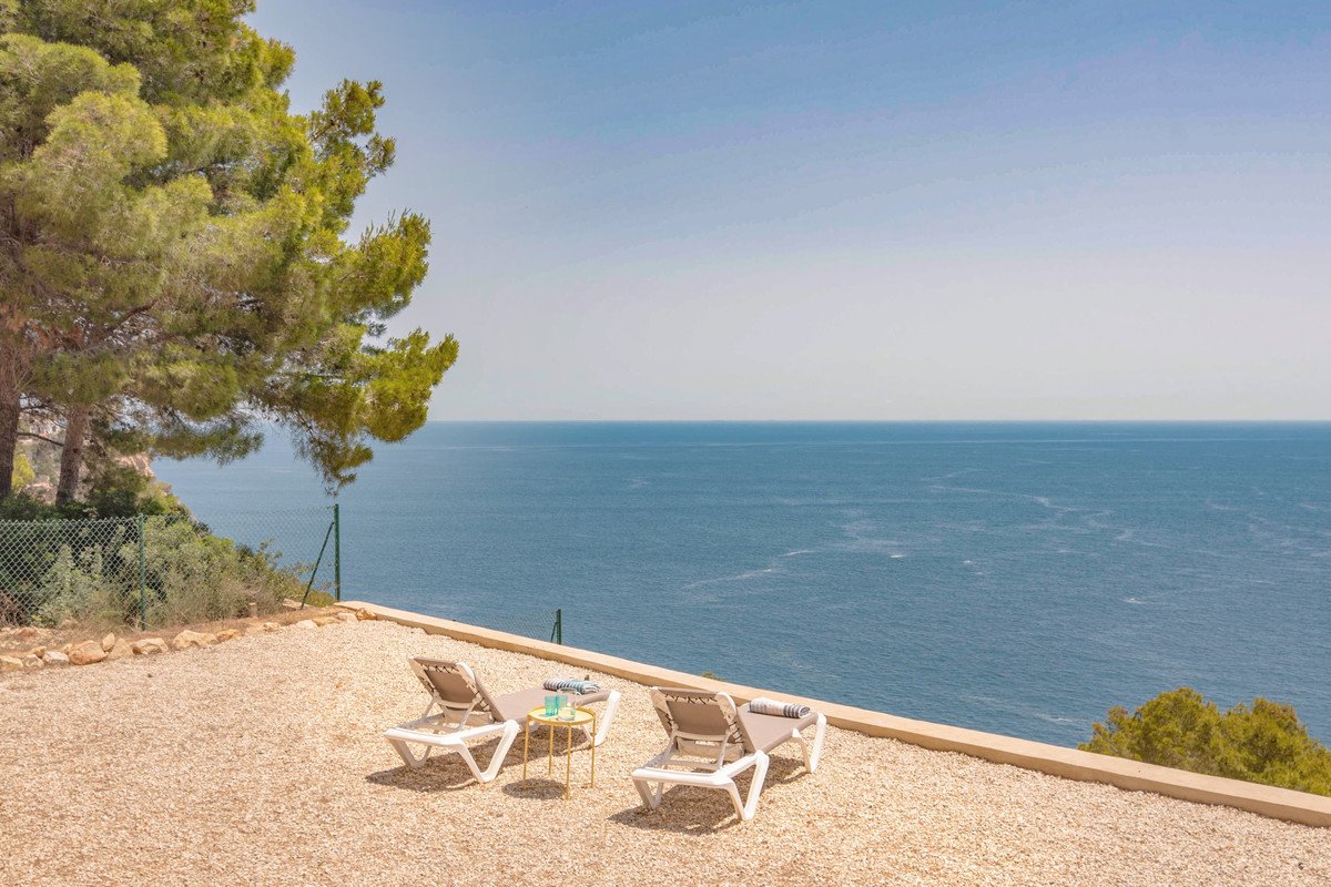 Terrace with two lounge chairs overlooking the beautiful blue sea and clear sky on a sunny day.